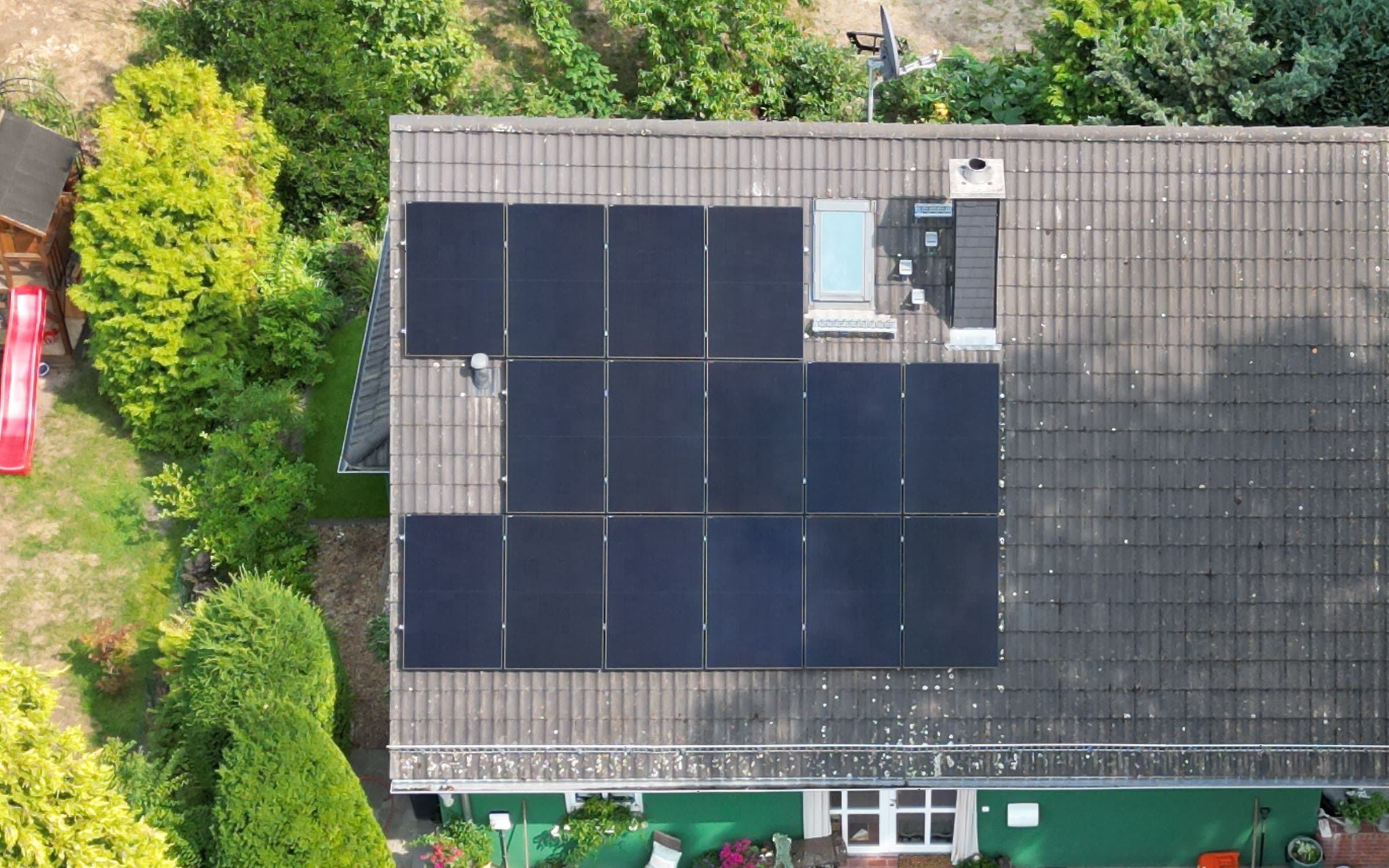 Dachfläche mit versetzt angeordneten PV-Modulen um Dachfenster und Schornstein, rechts fällt der Baumschatten sichtbar auf das Dach