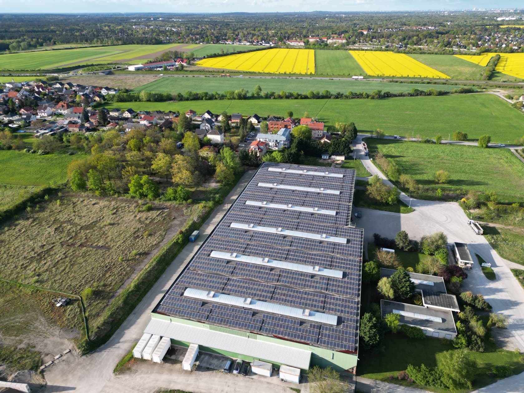 PV-Großanlage in Brandenburg: Hallendächer vor Dorf, Wiesen und Rapsfeldern